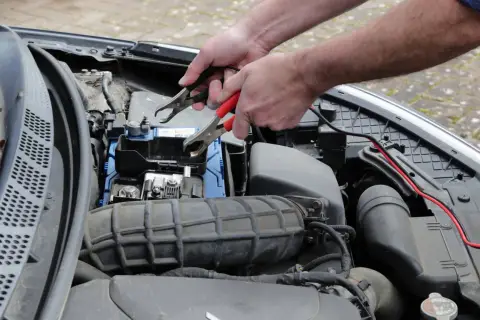 Ręce podłączają kable rozruchowe do akumulatora, bo diesel nie odpala za pierwszym razem.